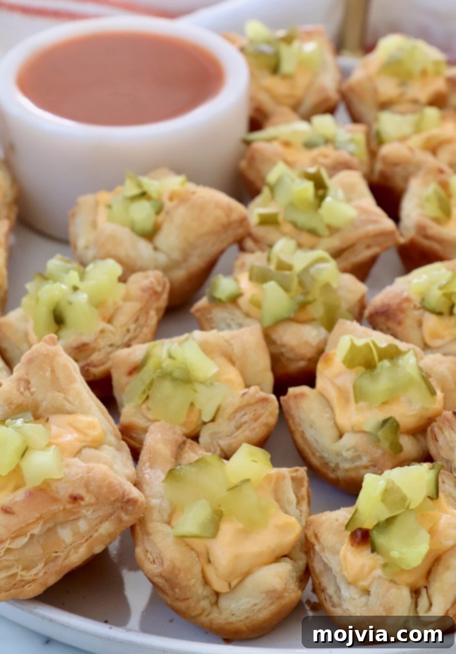 Dill Pickle Pastry Poppers 2 pickle puff pastry bites on a plate with a small bowl of buffalo sauce
