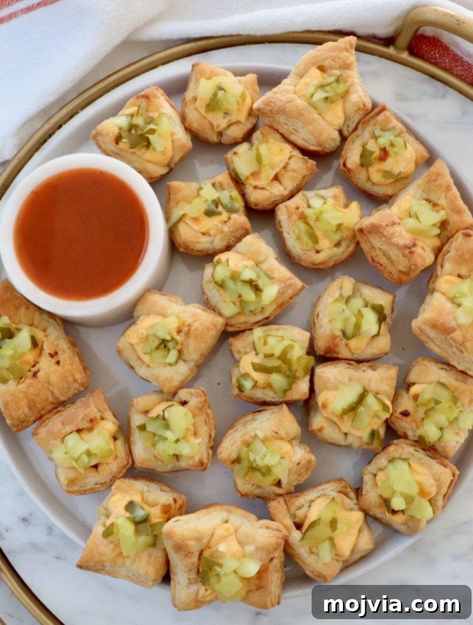 Dill Pickle Pastry Poppers 6 pickle puff pastry bites on a marble board with a small bowl of hot sauce