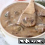 A close-up of mushroom gravy in a bowl with a spoon, ready to serve.