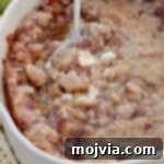 Baked apple pie dip in a baking dish with a serving spoon, garnished with a sprig of mint.