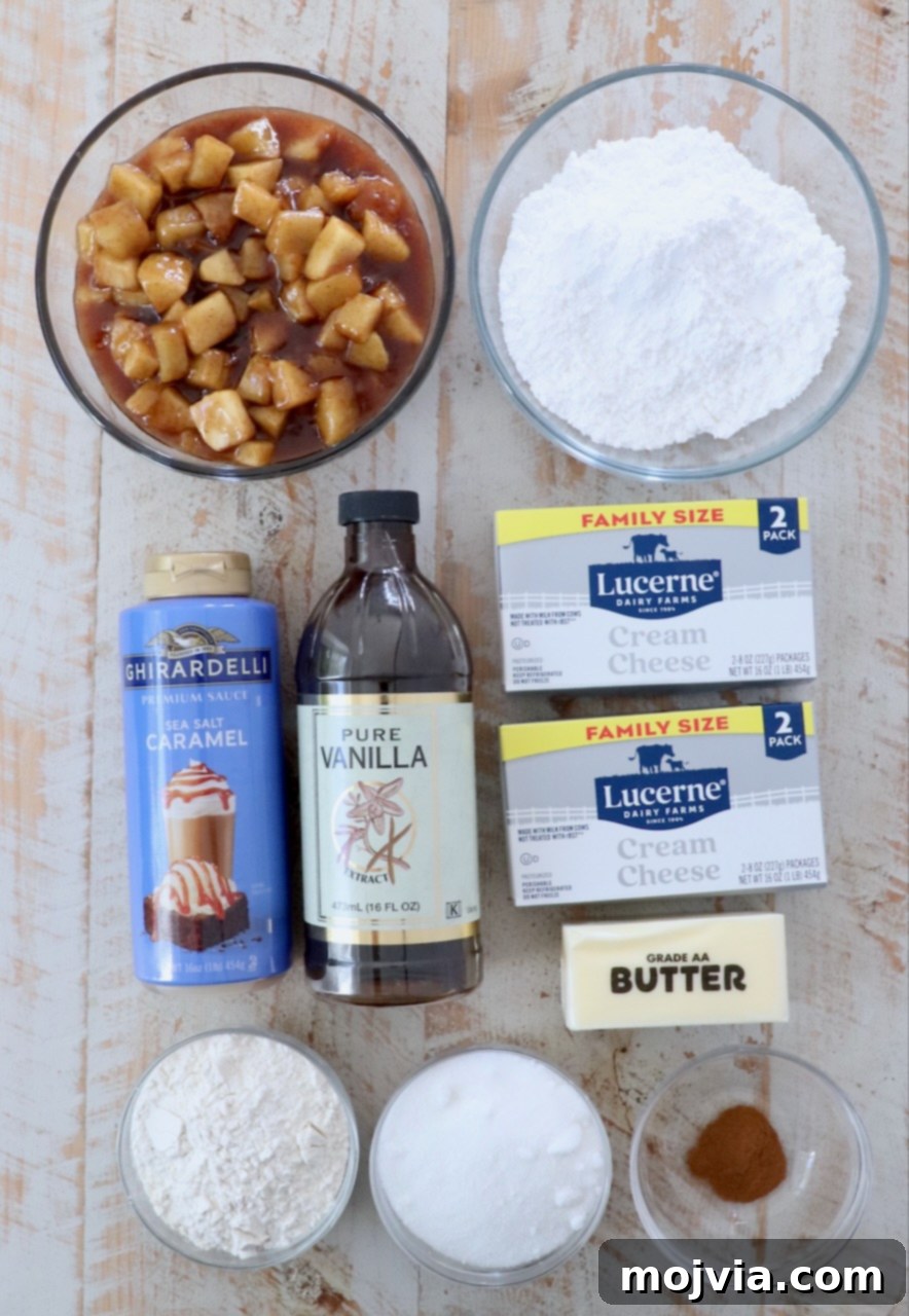 Various ingredients for an apple pie dip laid out on a white wooden board, including cream cheese, butter, apples, flour, cinnamon, and sugar.