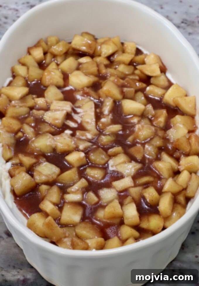 Spiced apple pie filling generously layered on top of the cream cheese base in a casserole dish.