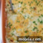 Ultimate Cheesy Potato Bake 12 au gratin potatoes in a casserole dish with a serving spoon
