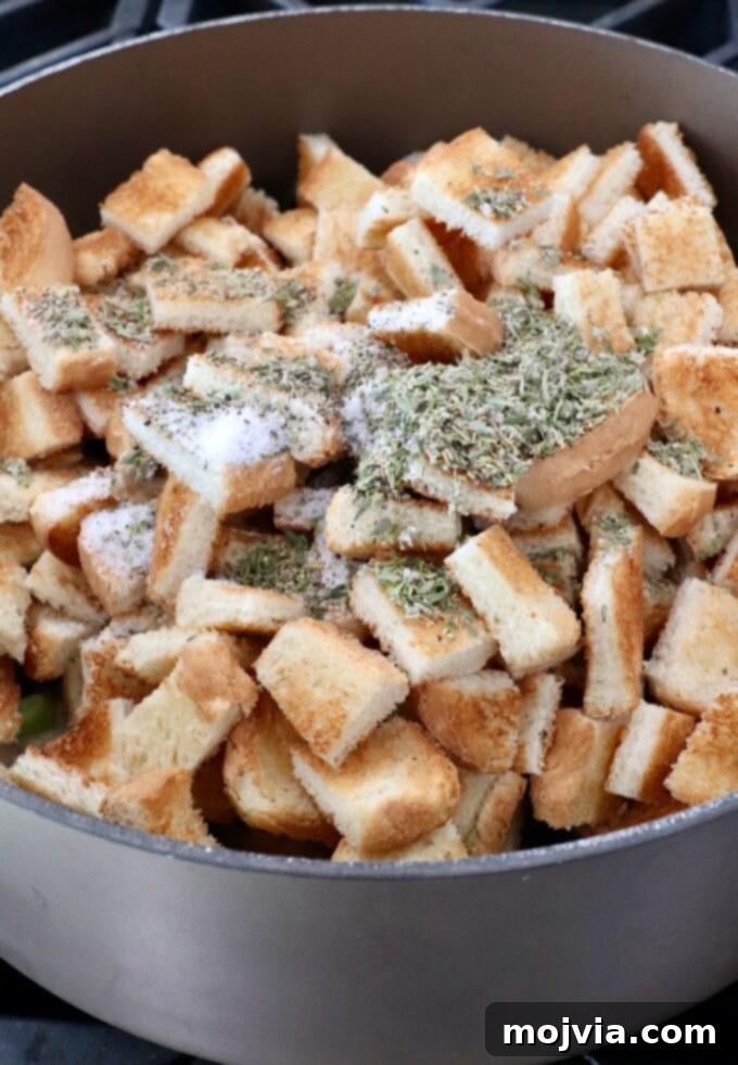 Umami Mushroom Stuffing 7 Toasted bread cubes combined with cooked vegetables and generously seasoned with a blend of salt, pepper, and dried herbs in a large pot.