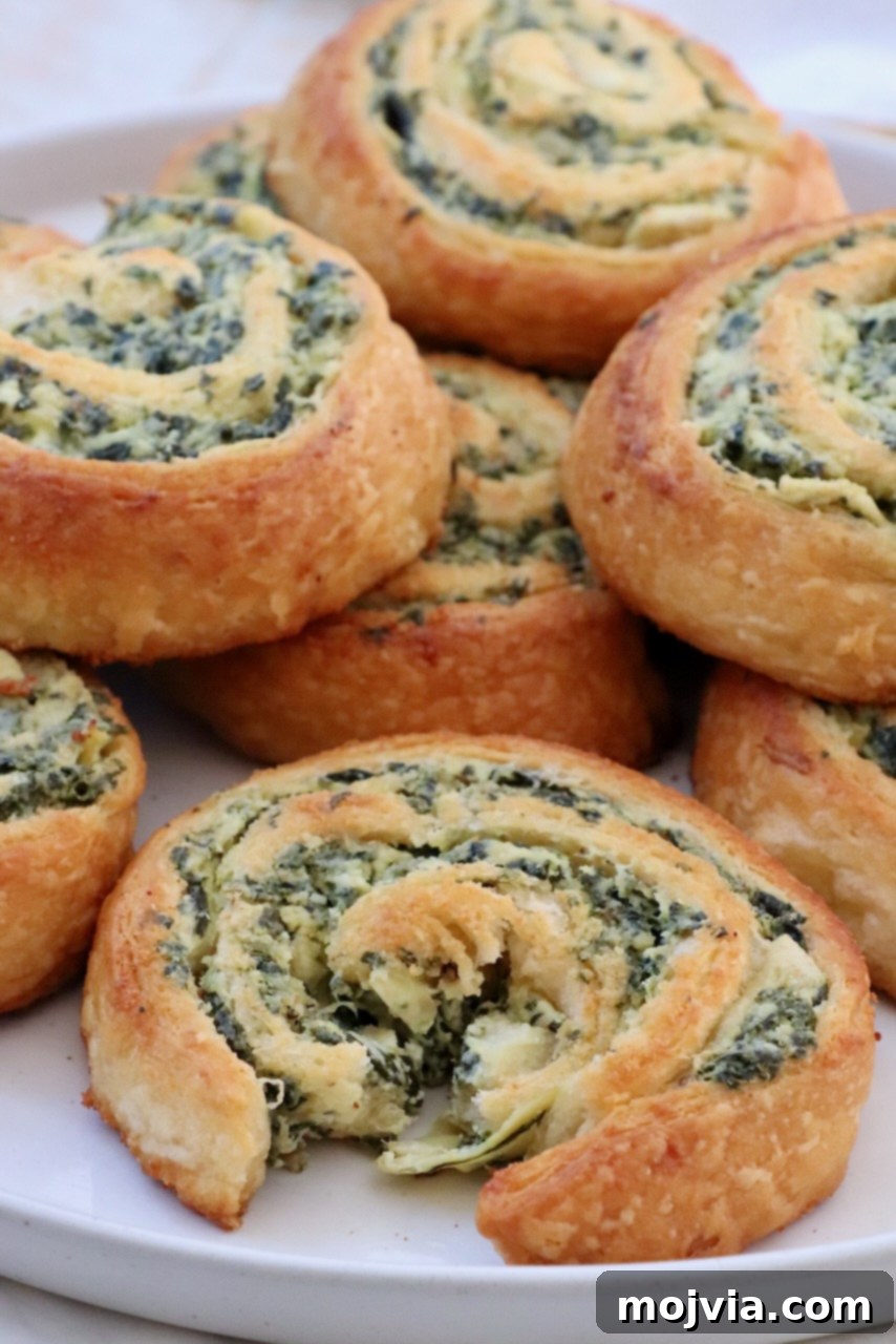 Savory Spinach Swirls 2 Stacked spinach dip rolls on a plate, showcasing their golden-brown exterior and creamy filling