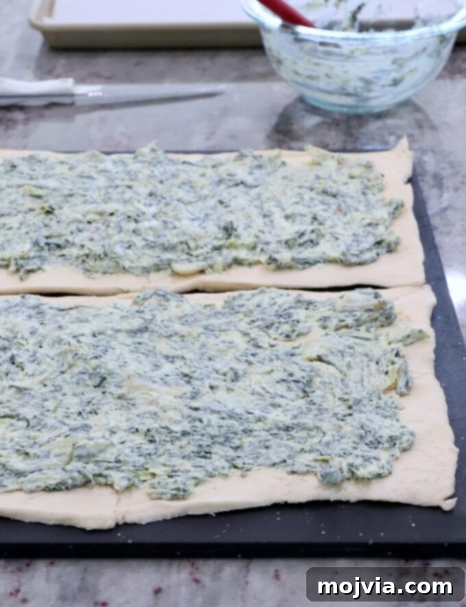 Savory Spinach Swirls 4 Spinach artichoke dip evenly spread on crescent roll dough on a cutting board, ready to be rolled