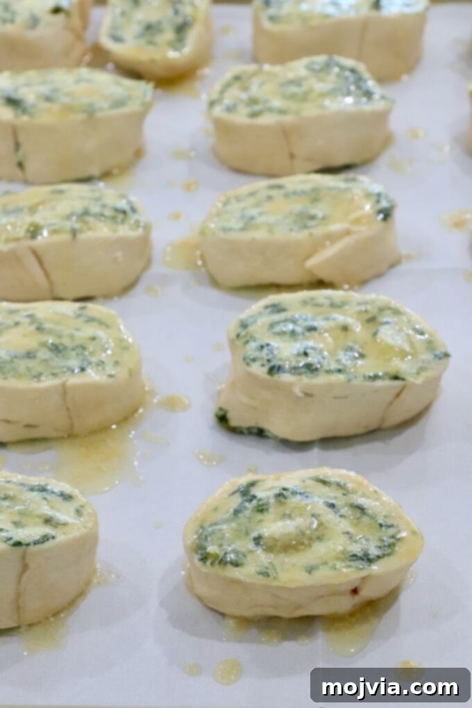 Savory Spinach Swirls 6 Spinach artichoke rolls brushed with melted garlic butter on a baking sheet, preparing for the oven