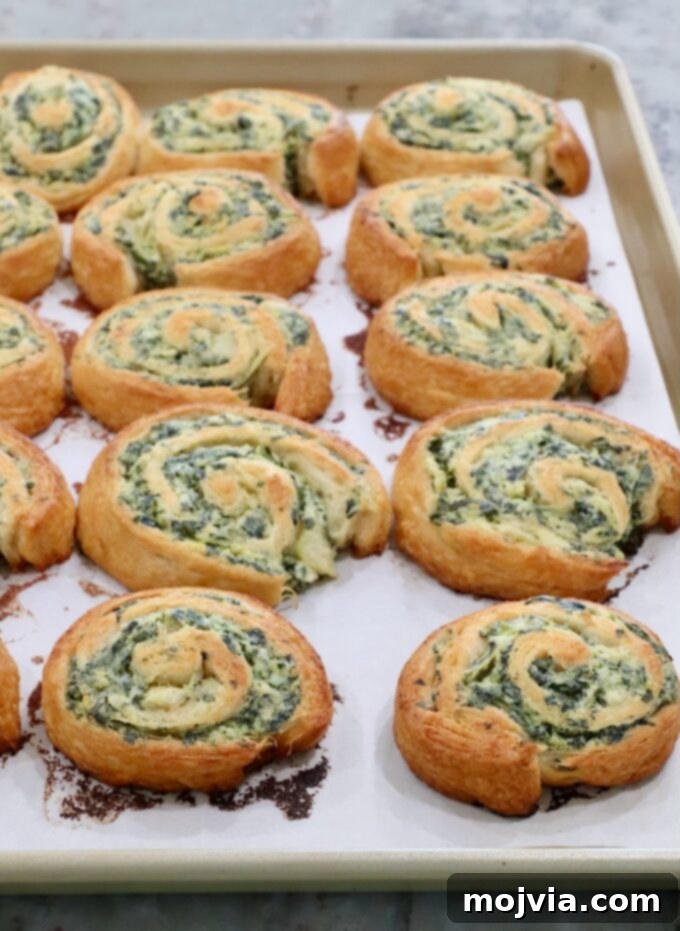 Savory Spinach Swirls 7 Freshly baked spinach pinwheels on a baking sheet, golden brown and perfectly cooked