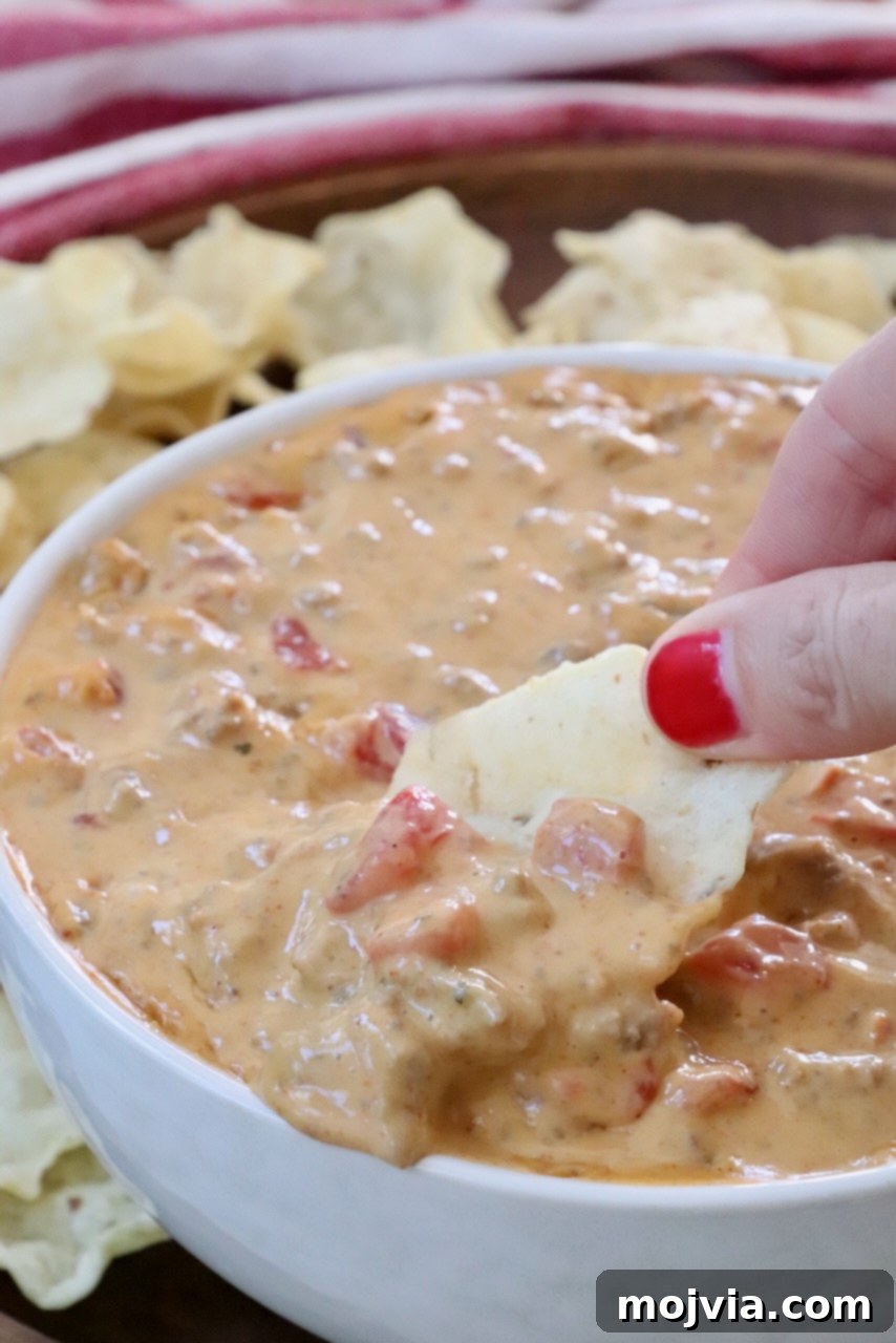 Irresistible Party Queso 2 hand dipping a tortilla chip into rotel dip in a bowl