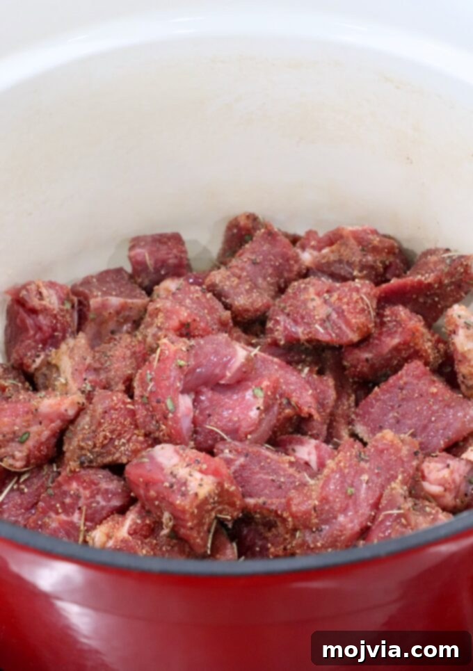 Raw, seasoned, cubed beef ready for searing in a large Dutch oven
