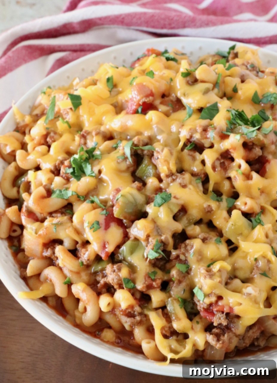 Prepared American Goulash in a bowl, generously topped with shredded cheddar cheese and a sprinkle of fresh parsley, showcasing its rich, comforting appeal.