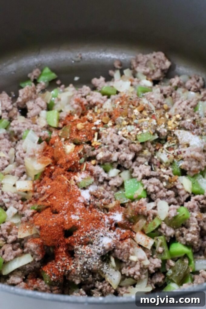Cooked ground beef mixed with sautéed vegetables, seasoned with paprika, Italian seasoning, salt, pepper, and Worcestershire sauce in a large pot.