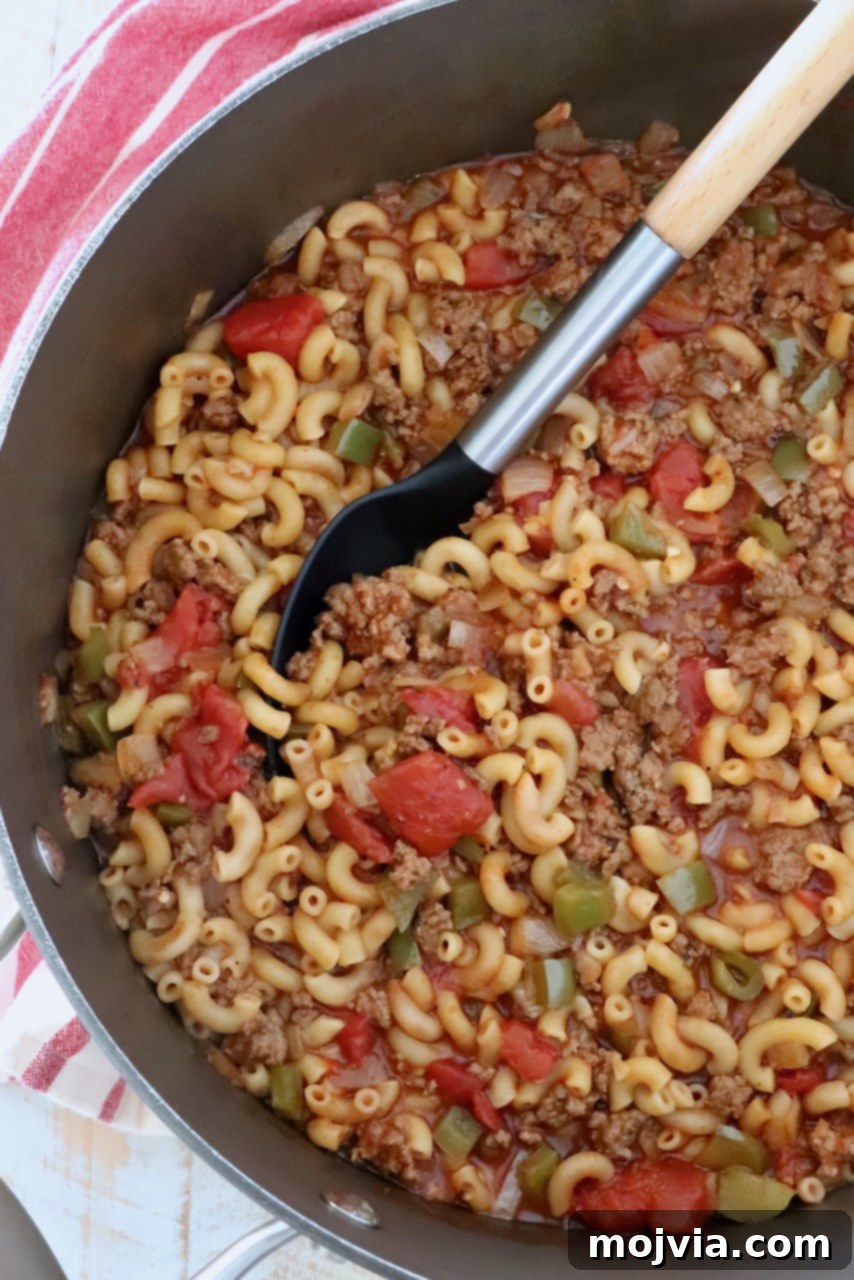 Ground beef goulash simmering in a large pot, with a serving spoon nestled in the rich, cheesy mixture, ready to be dished out.