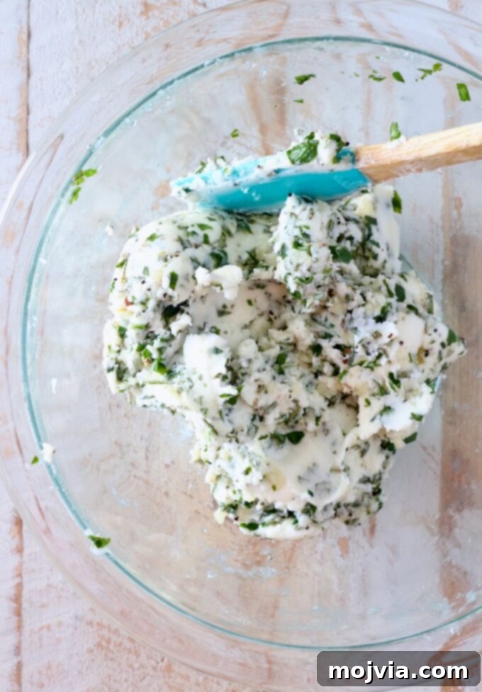 Butter Infusions 5 garlic herb compound butter mixed together in a glass bowl with a spatula