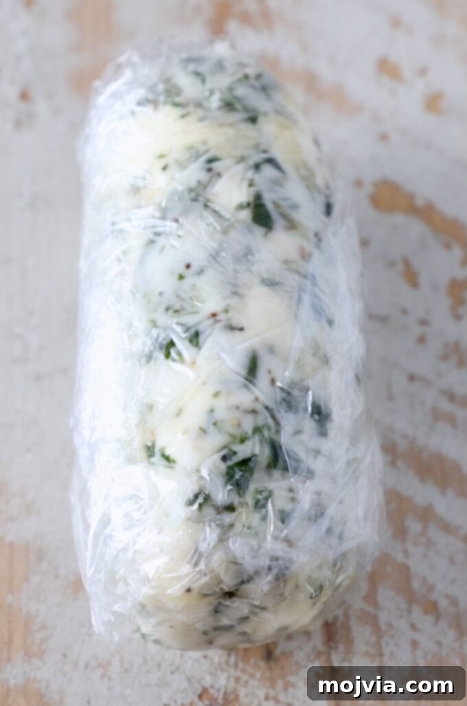 Butter Infusions 6 compound butter wrapped up in plastic wrap on a white wood board