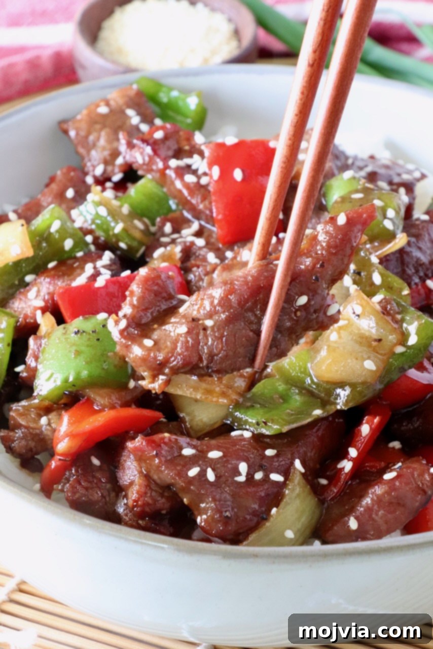 chopsticks holding a piece of steak over a bowl of cooked steak and peppers