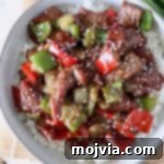 cooked steak and peppers in sauce over cooked white rice in a bowl topped with sesame seeds