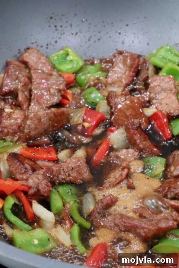 cooked beef, diced bell peppers and onions mixed together in a large wok with sauce
