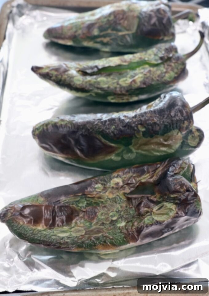 Roasted Poblano Chicken Soup 5 Roasted poblano peppers with charred and bubbling skin on a foil-lined baking sheet after broiling.