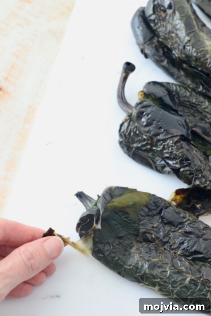 Roasted Poblano Chicken Soup 7 A hand carefully peeling the charred skin from a roasted poblano pepper on a cutting board.