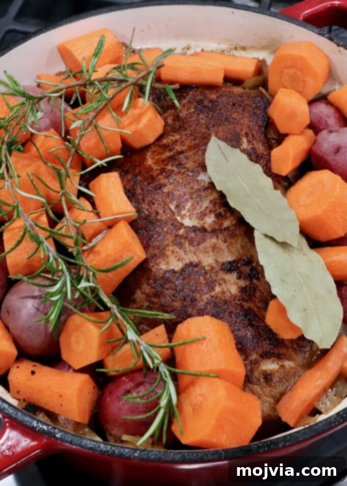 seared pork shoulder in a large pot with diced carrots, potatoes, bay leaves and rosemary