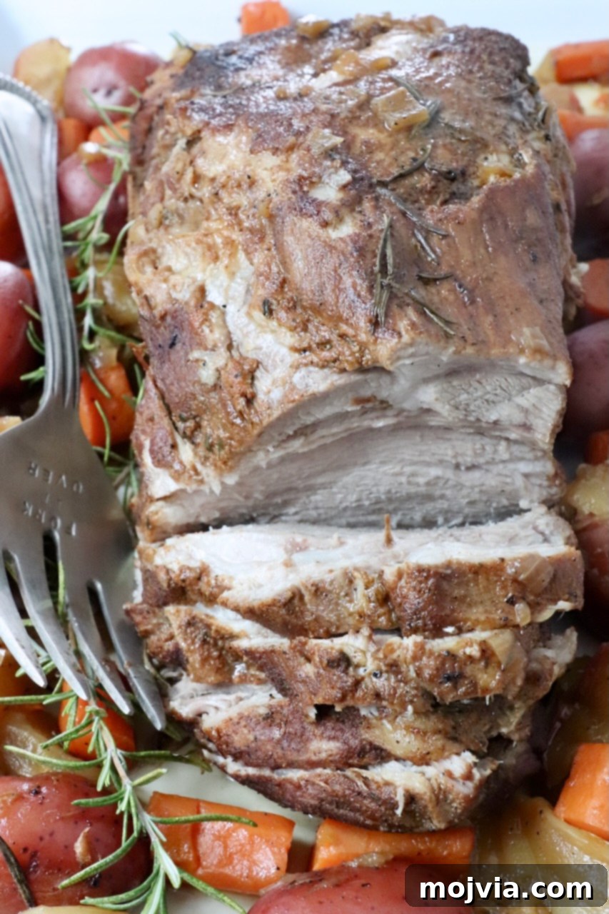 pork roast partially sliced on a serving plate with a large fork and roasted vegetables