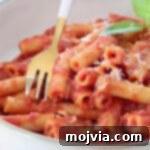 Cooked ziti pasta tossed in tomato nduja sauce in a bowl with a fork, ready to be enjoyed
