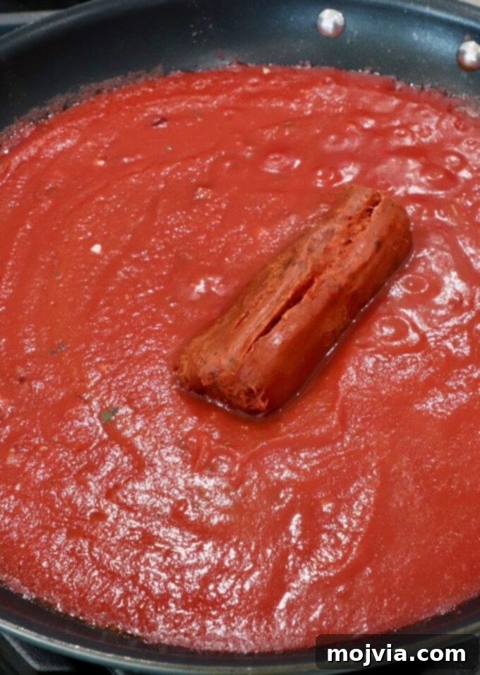 Fiery Nduja Tomato Sauce 6 Spreadable nduja sausage being added to the simmering tomato sauce in a skillet, ready to melt and infuse its spicy flavor