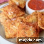 toasted raviolis stacked up on a plate with a small bowl of marinara sauce on the plate