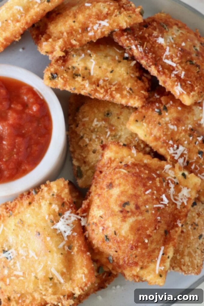 toasted raviolis stacked up on a plate with a small bowl of marinara sauce on the side