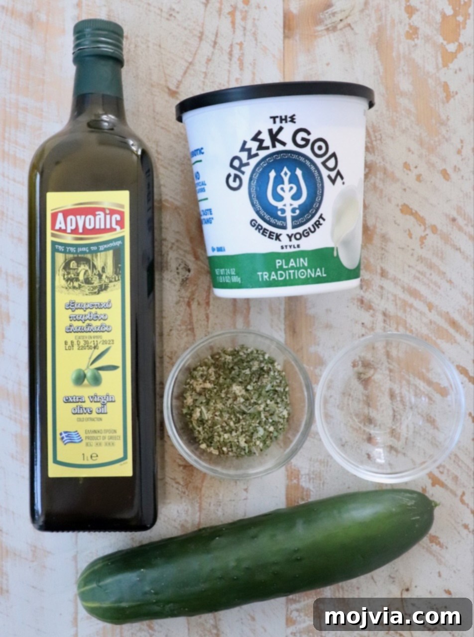 Creamy Greek Cucumber Garlic Dip 3 A beautiful display of fresh ingredients for Tzatziki Sauce, including cucumber, Greek yogurt, olive oil, and herbs, arranged on a rustic white wood board.
