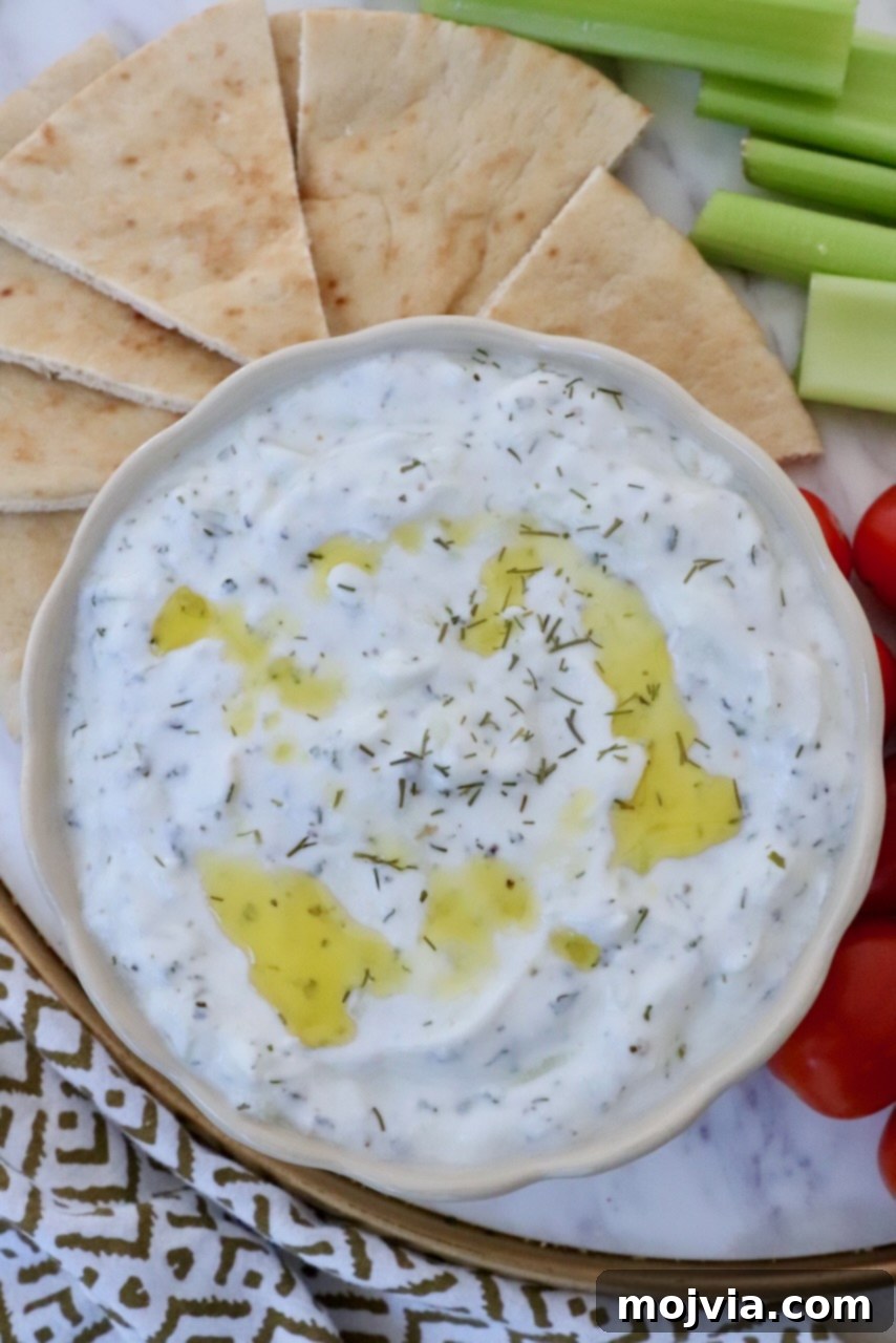 Creamy Greek Cucumber Garlic Dip 7 A bowl of fresh tzatziki dip generously drizzled with olive oil, surrounded by artfully arranged sliced pita bread and a medley of fresh vegetables on the side, inviting you to dip and enjoy.