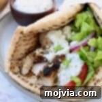 Greek Style Chicken Gyros 10 pita bread filled with chicken gyros meat, tzatziki sauce, shredded lettuce, sliced onions and tomatoes, on a plate