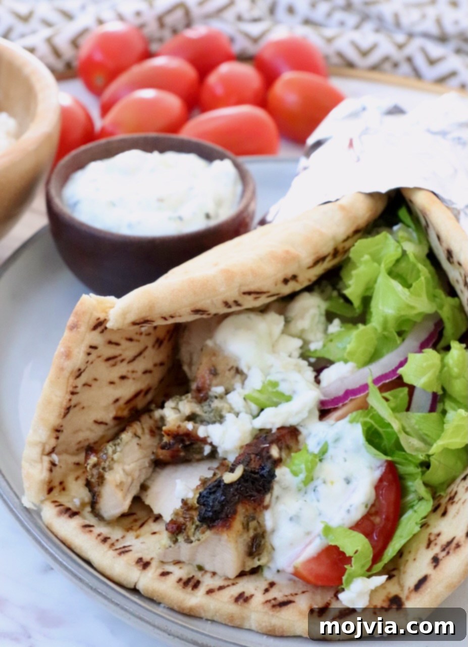 Greek Style Chicken Gyros 9 pita bread filled with chicken gyros meat, tzatziki sauce, shredded lettuce, sliced onions and tomatoes, on a plate