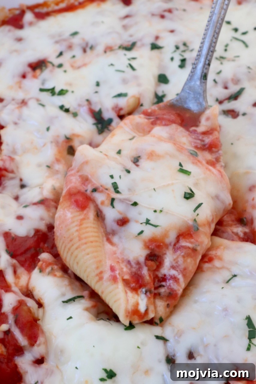 Cheesy Baked Stuffed Shells 2 stuffed pasta shell filled with cheese and marinara sauce lifted out of a casserole dish with a serving spoon