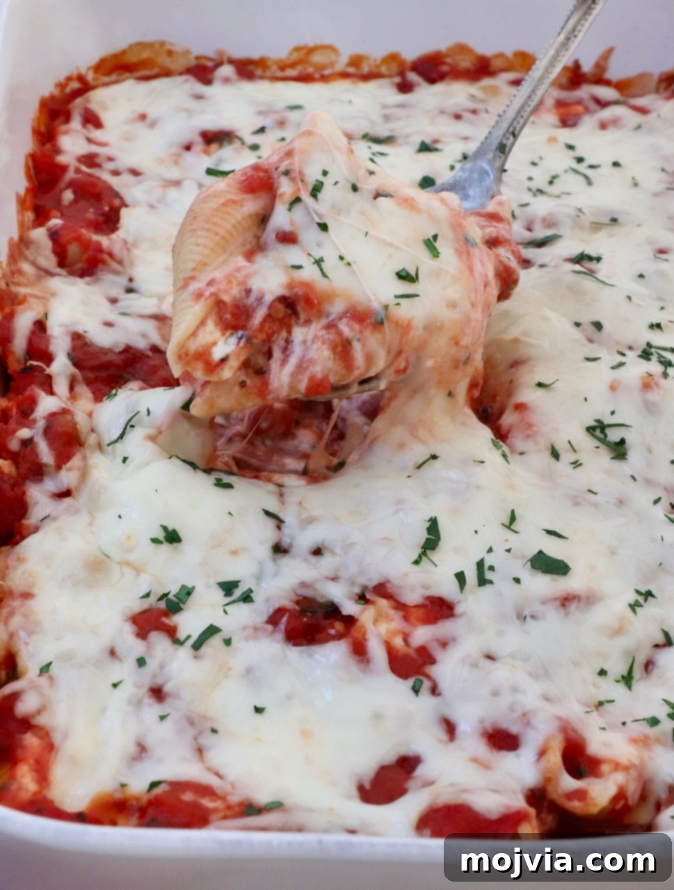 Cheesy Baked Stuffed Shells 11 one cheese stuffed pasta shell lifted out of a casserole dish full of stuffed shells with a large spoon