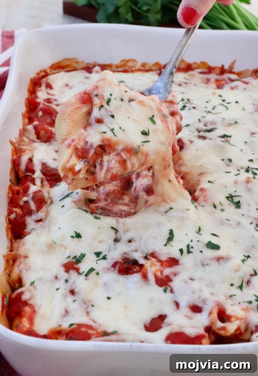Cheesy Baked Stuffed Shells 10 cheese filled stuffed pasta shell lifted out of a casserole dish with a serving spoon