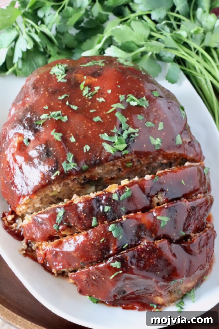 Golden Air Fryer Meatloaf 2 Glazed, cooked air fryer meatloaf, partially sliced on a plate with fresh parsley garnish