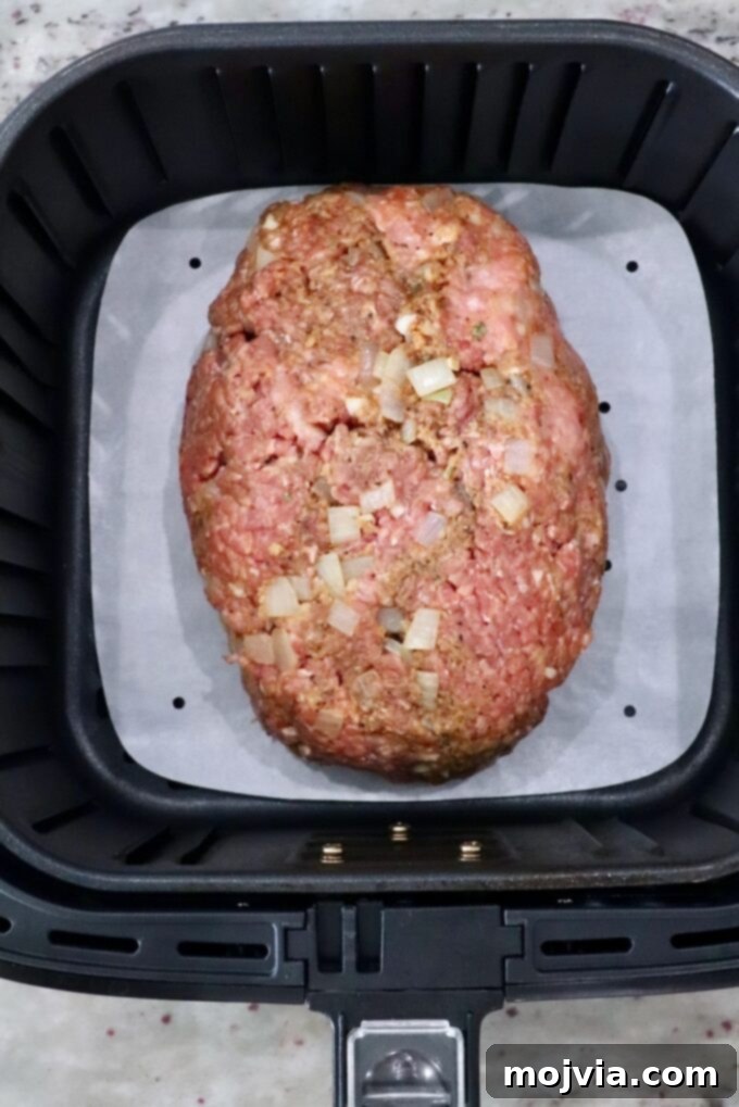 Golden Air Fryer Meatloaf 6 Uncooked meatloaf in an air fryer basket with a parchment paper liner