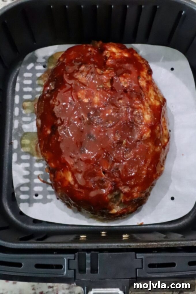 Perfect Air Fryer Meatloaf 8 cooked, glazed meatloaf in an air fryer basket with a parchment paper liner