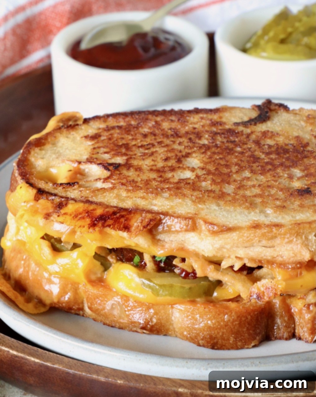 meatloaf sandwich on a plate with a small bowl of bbq sauce and small bowl of pickles behind the sandwich