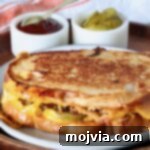 meatloaf sandwich on a plate with small bowls of bbq sauce and pickles behind it