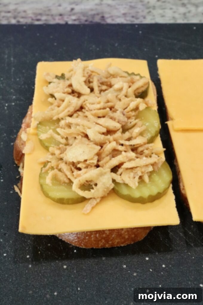 sliced cheese, pickles, and fried onion strings, on top of sliced bread on a cutting board