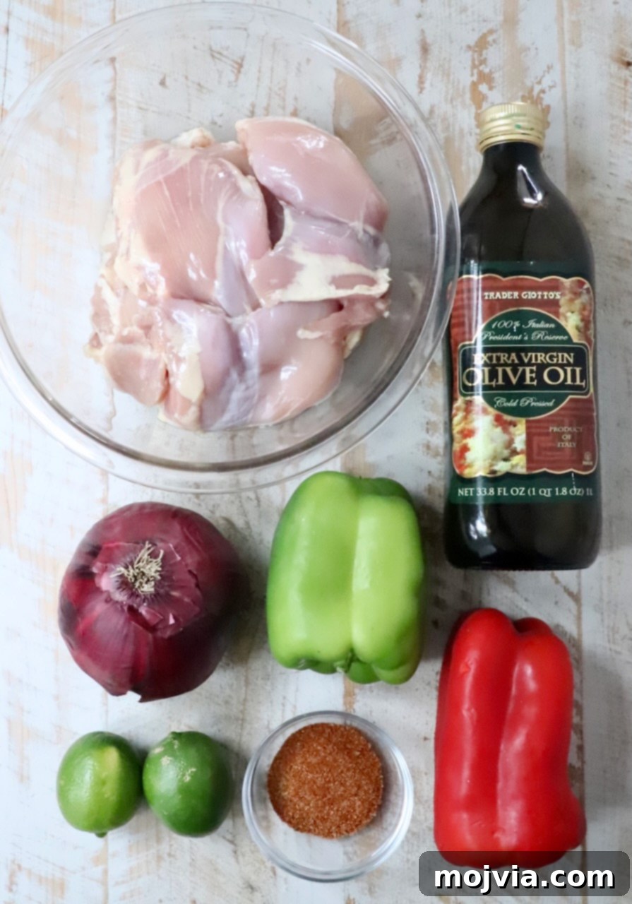 Sizzling Air Fryer Chicken Fajitas 3 A vibrant selection of fresh ingredients laid out on a white wooden board, including boneless chicken thighs, colorful bell peppers, a red onion, lime, olive oil, and a bowl of homemade fajita seasoning, ready for making air fryer chicken fajitas.