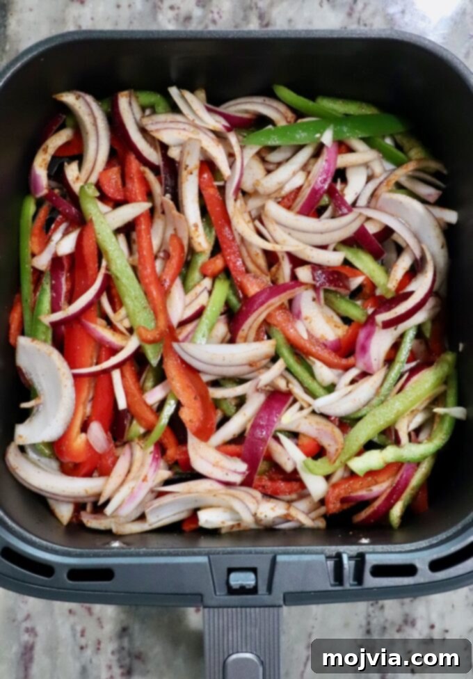 Sizzling Air Fryer Chicken Fajitas 7 Freshly sliced bell peppers and red onions evenly distributed in an air fryer basket, ready to be cooked until tender-crisp.