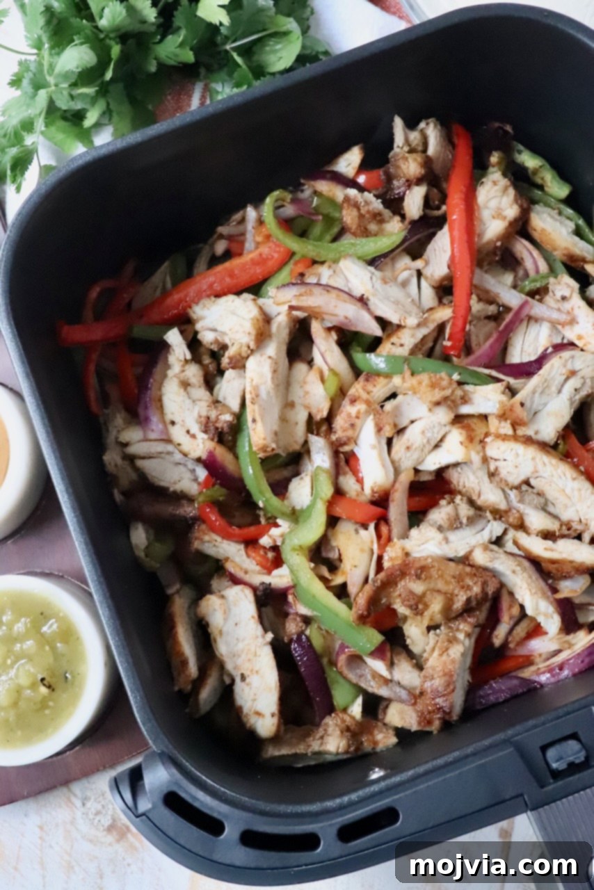 Sizzling Air Fryer Chicken Fajitas 9 Close-up of cooked, sliced chicken fajita thighs and perfectly tender-crisp bell peppers and onions, all mixed together and glistening in an air fryer basket, ready for serving.