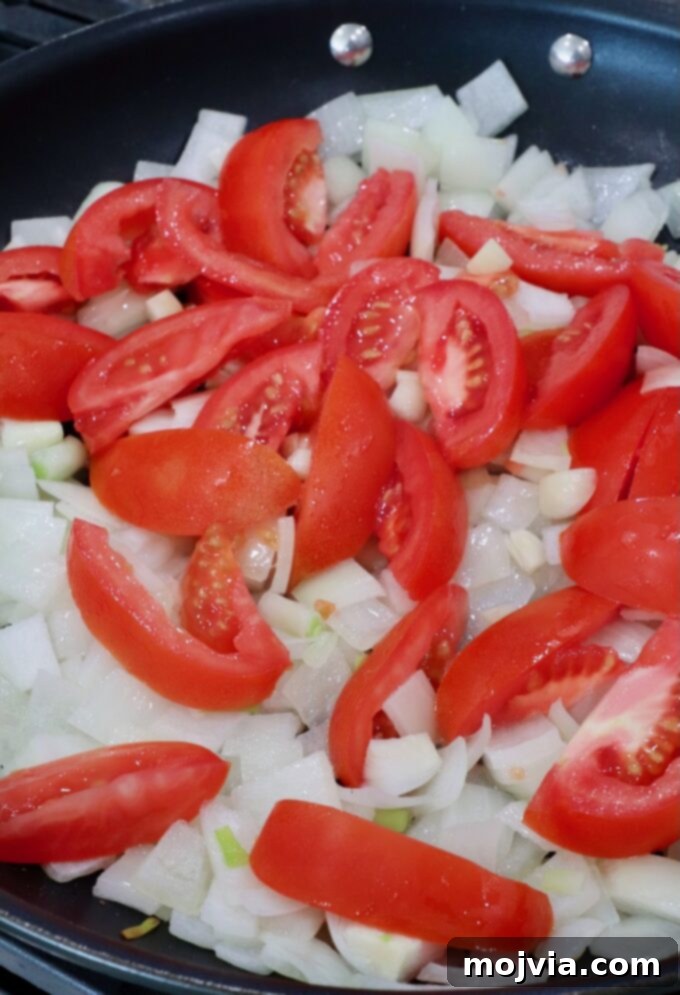 Diced onions and sliced tomatoes sautéing in a skillet