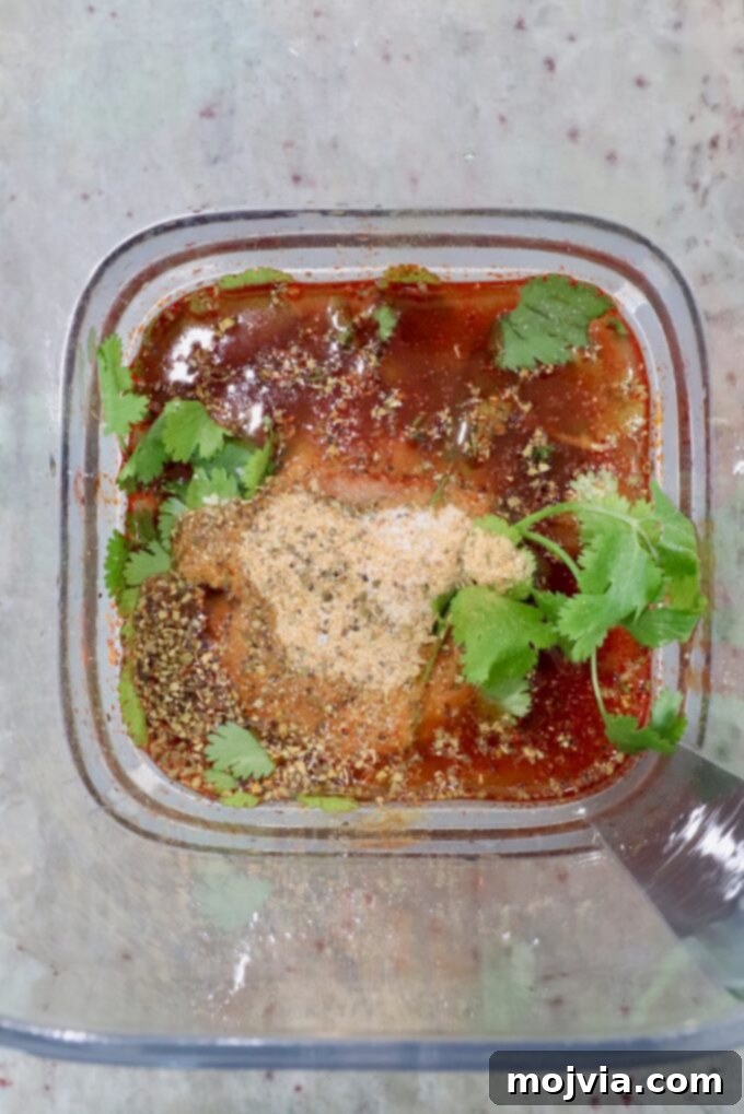 Adobo sauce ingredients in a blender, topped with spices and fresh cilantro