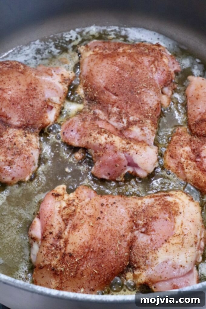 Raw, seasoned chicken thighs in a large Dutch oven on the stove