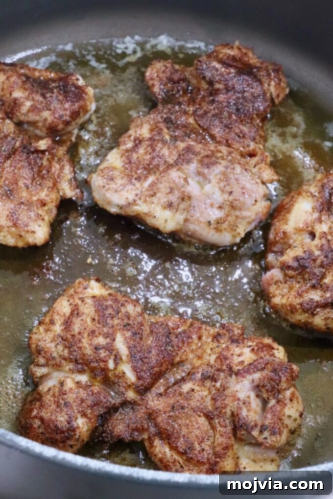 Seasoned chicken thighs searing in a large Dutch oven